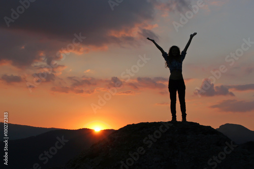 Silhouette of a girl standing on a mountain with his hands up ag © zatvorniknik