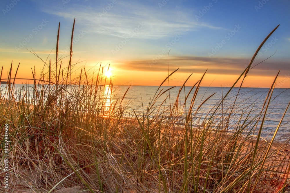Fotka „Dawn Of A New Day.Beautiful sunrise illuminates sand dunes and the  blue water horizon as a new day begins. Port Austin, Michigan.“ ze služby  Stock | Adobe Stock