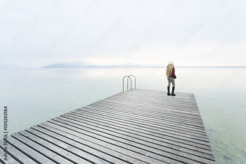 Young woman with long blond hair with hat on the dock of a lake