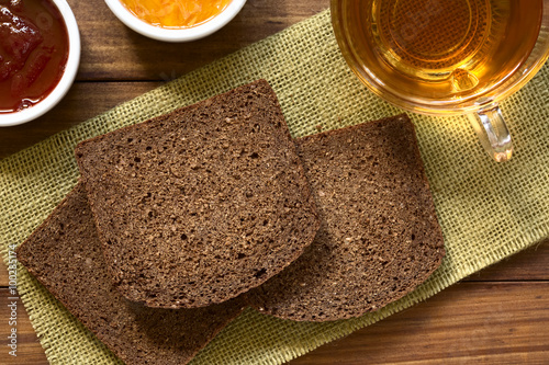 Slices of pumpernickel dark rye bread with strawberry and orange jam, cup of tea on the side, photographed overhead with natural light (Selective Focus, Focus on the upper slice) photo