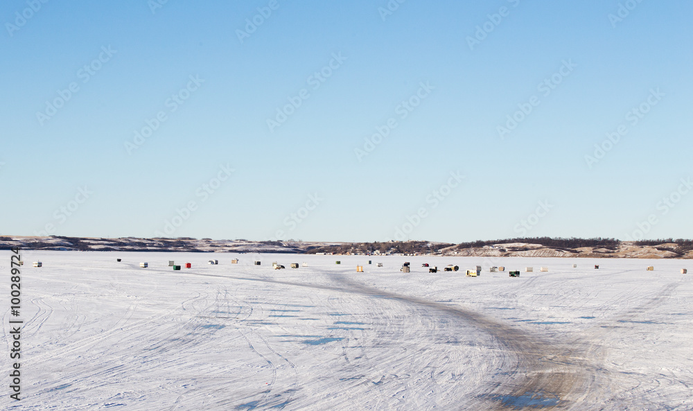 Groups of multiple ice fishing shacks on a snow covered lake in a winter landscape