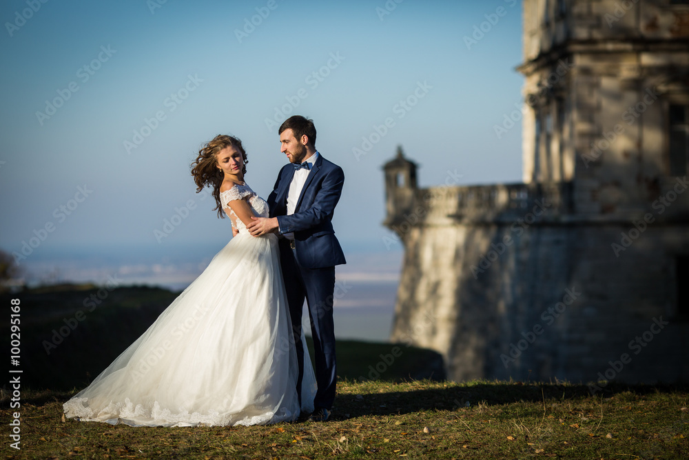 Sensual happy couple posing and hugging near old castle at sunset with a beautiful skyline background