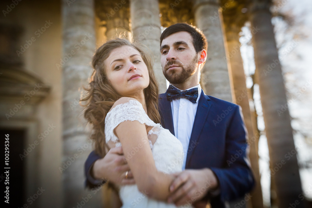 Sensual romantic newlywed bride and groom hugging in front of old baroque church with columns at sunset closeup