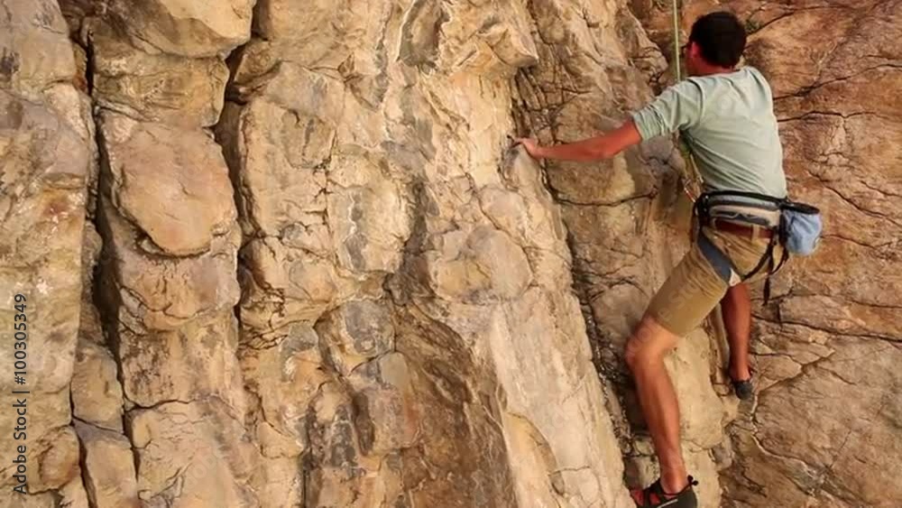 Handheld shot of a rock climber carefully making his way up a cliff. Handheld shot of a rock climber carefully making his way up a cliff.