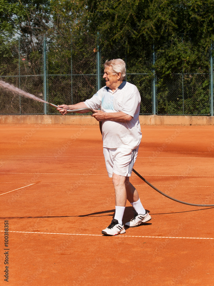 Senior men sprinklig tennis court before playing