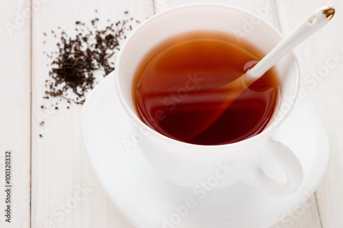 tea in a white mug with a spoon and tea leaves on a white background