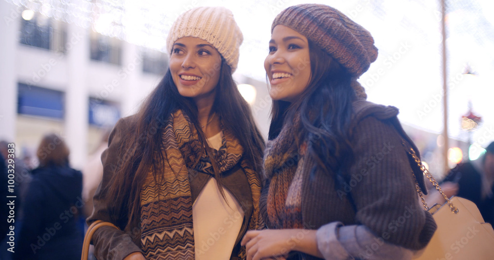 Two stylish attractive young women standing chatting in an urban street in fashionable winter outfits  closeup upper body panoramic view