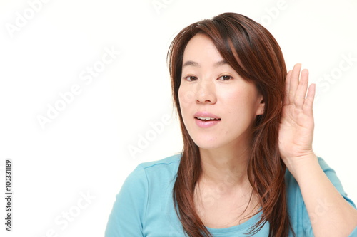 Japanese woman with hand behind ear listening closely