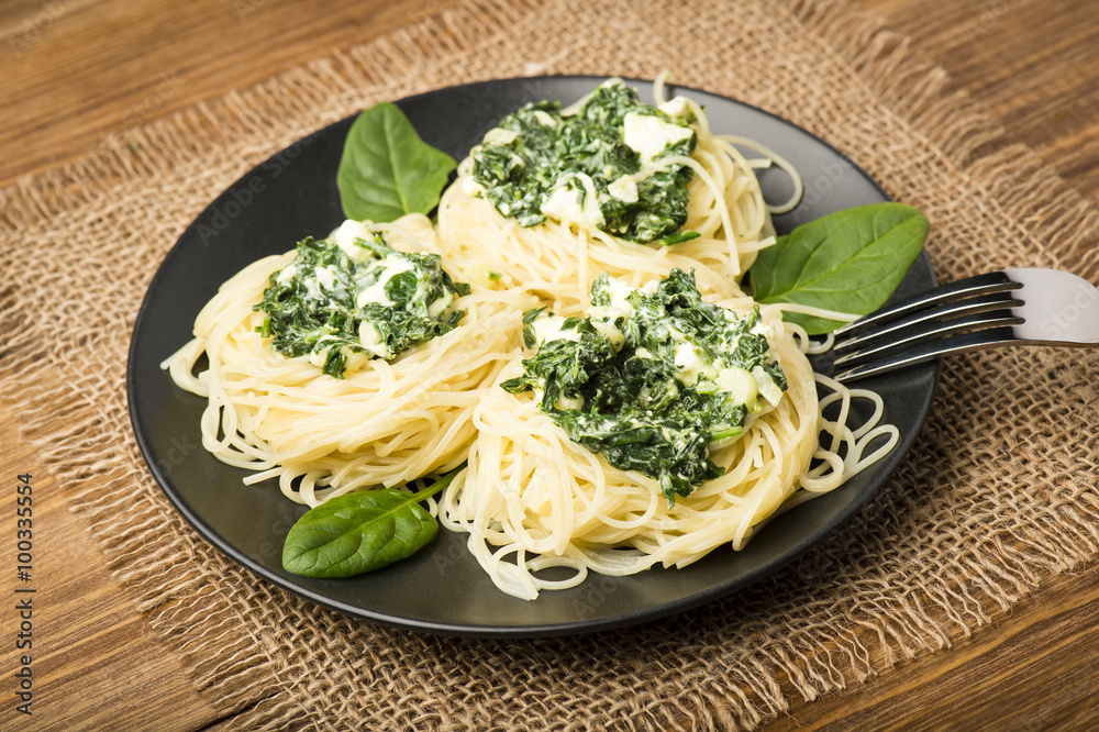 Italian pasta with spinach and feta on black plate on the wooden background.