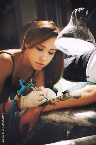 Beautiful young girl tattoo artist portrait during creation tattoo on a man`s hand.
