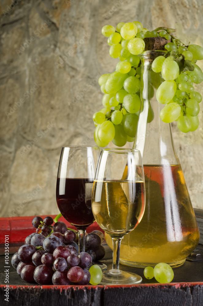 Still life with ripe grapes, wine glasses and wine bottles in old cellar