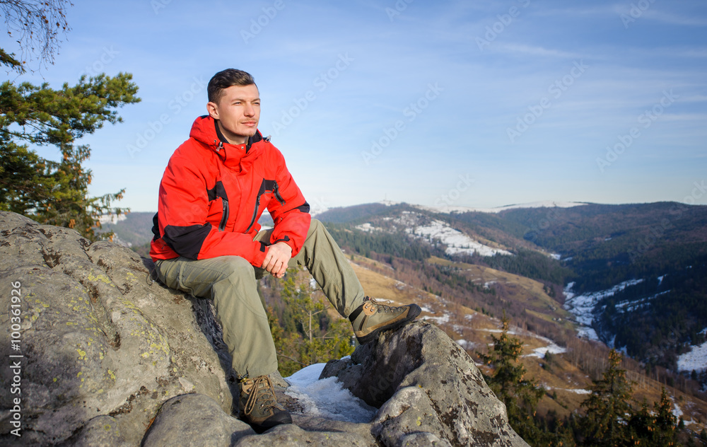 Young tourist sitting on top of the mountain and looking into di Young tourist sitting on top of the mountain and looking into di
