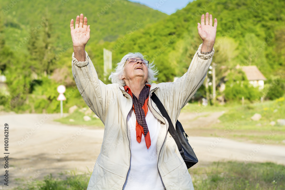 healthy elderly woman looking up with arms outstretched in the mountain