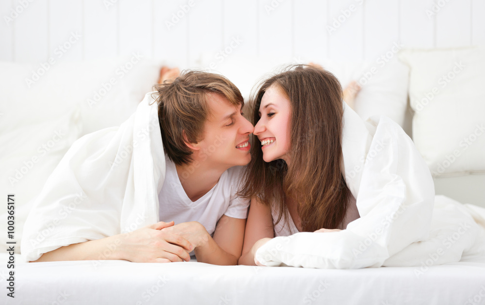 Happy couple laughing in bed peeking out from under blanket Happy couple laughing in bed peeking out from under blanket
