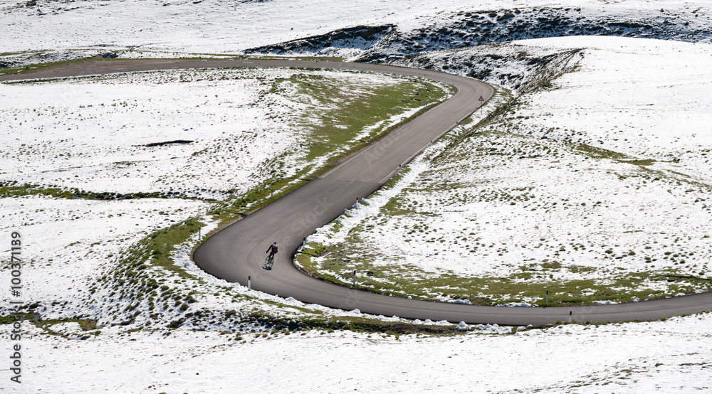 Obraz premium Cyclist goes downhill along a mountain road in a snowy landscape. Dolomites, Italy, Europe.