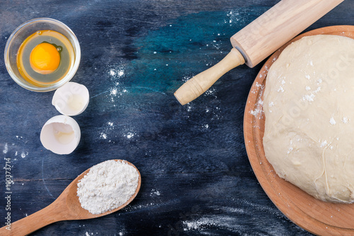 Dough, egg, flour and rolling pin. Selective focus. Top view. Rustic background.