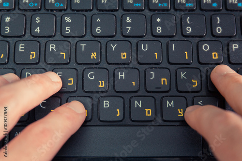 Man typing on a keyboard with letters in Hebrew and English - Laptop keyboard - Top View - Close up