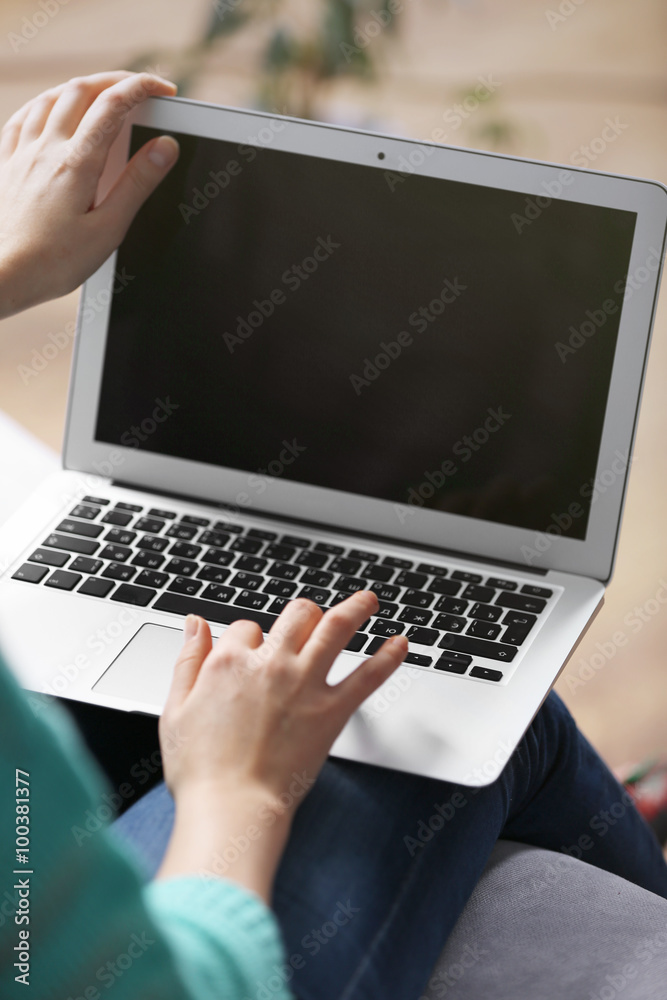 Woman sitting on sofa with a laptop on her knees in a room