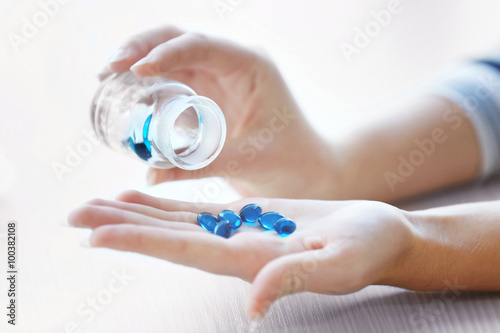 Woman spills blue medical capsules to her hand, close up