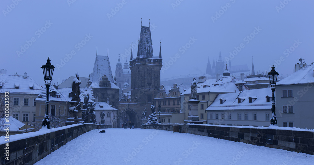 Obraz premium Early Morning snowy Prague Lesser Town with gothic Castle, Bridge Tower and St. Nicholas' Cathedral from Charles Bridge with its Statues, Czech republic