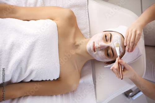 Spa concept. Young woman with facial mask in beauty salon, close up