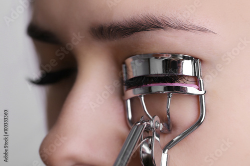 Woman corrects eyelashes with curling tongs, close up photo