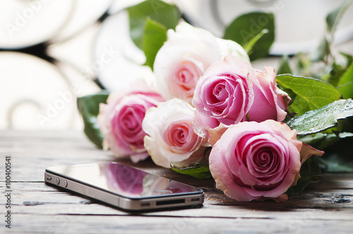 Pink roses and smartphone on the wooden table