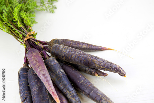 Bunch of heirloom purple carrots, over white and wooden backgrou