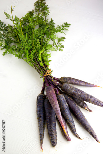 Bunch of heirloom purple carrots, over white and wooden backgrou