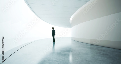 Young businessman wearing suit and stands in the open space interior. Wide