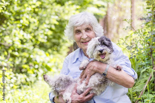 Obraz na płótnie beautiful Senior smiling woman hugging her small white poodle dog in the mountai