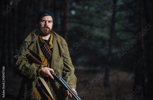 brutal hunter, bearded man in warm hat with a gun in his hand 