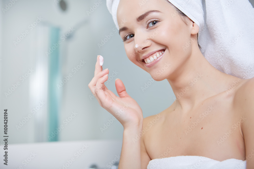 Young Woman Wrapped with Bath Towels, Applying Cream on her Face Young Woman Wrapped with Bath Towels, Applying Cream on her Face