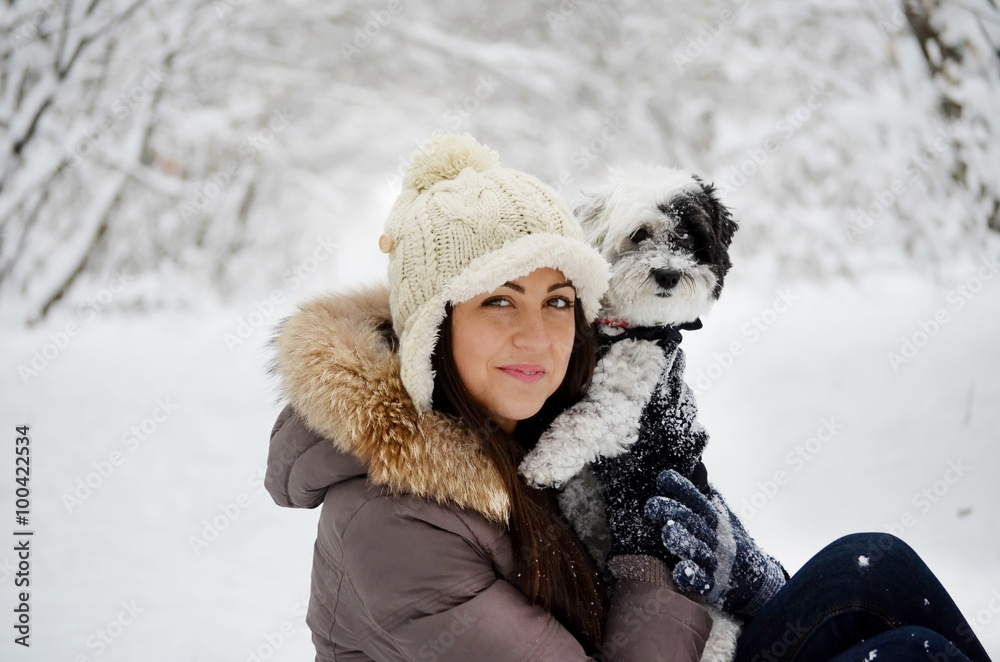 Fototapeta premium Young beautiful woman smiling and hugging her dressed white poodle dog.Winter time