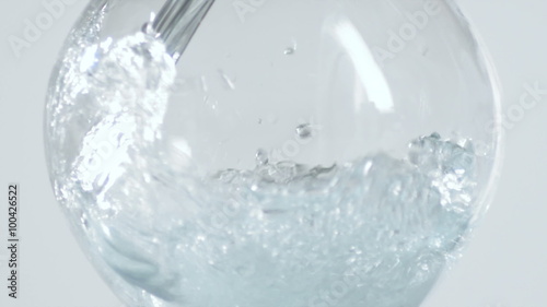 Water curls off the curved side of a fish bowl shaped glass in slow motion as container fills