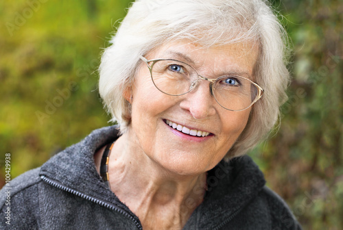  Seniorin lächelt entspannt und glücklich vor Naturhintergrund draußen