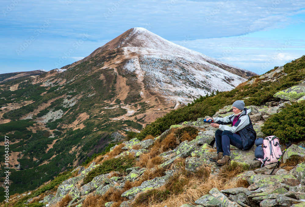 Fototapeta premium Female Hiker sitting on green Stone and using Thermos
