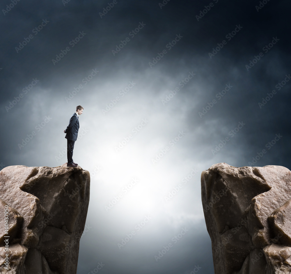 Young businessman standing on edge of rock mountain and looking