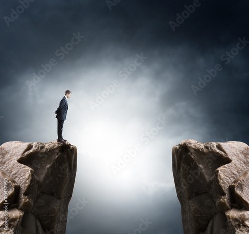 Obraz na plátne Young businessman standing on edge of rock mountain and looking