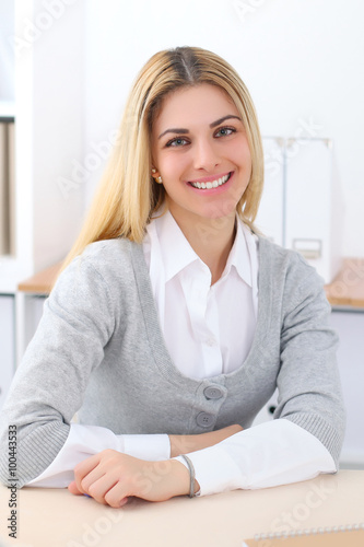 Portrait of young business woman sitting at the desk on office background