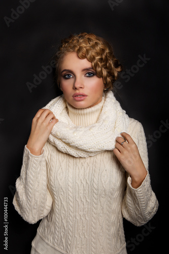 portrait of a beautiful young blonde woman on dark background. hair tied in a braid. girl wearing a warm sweater and scarf. copy space. photo