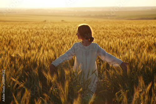 Happy young woman among field at sunset