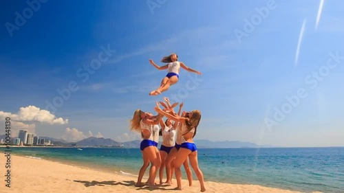 cheerleaders in uniform perform Toe Touch Toss on beach