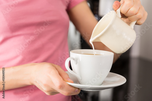 Woman adding milk to her coffee