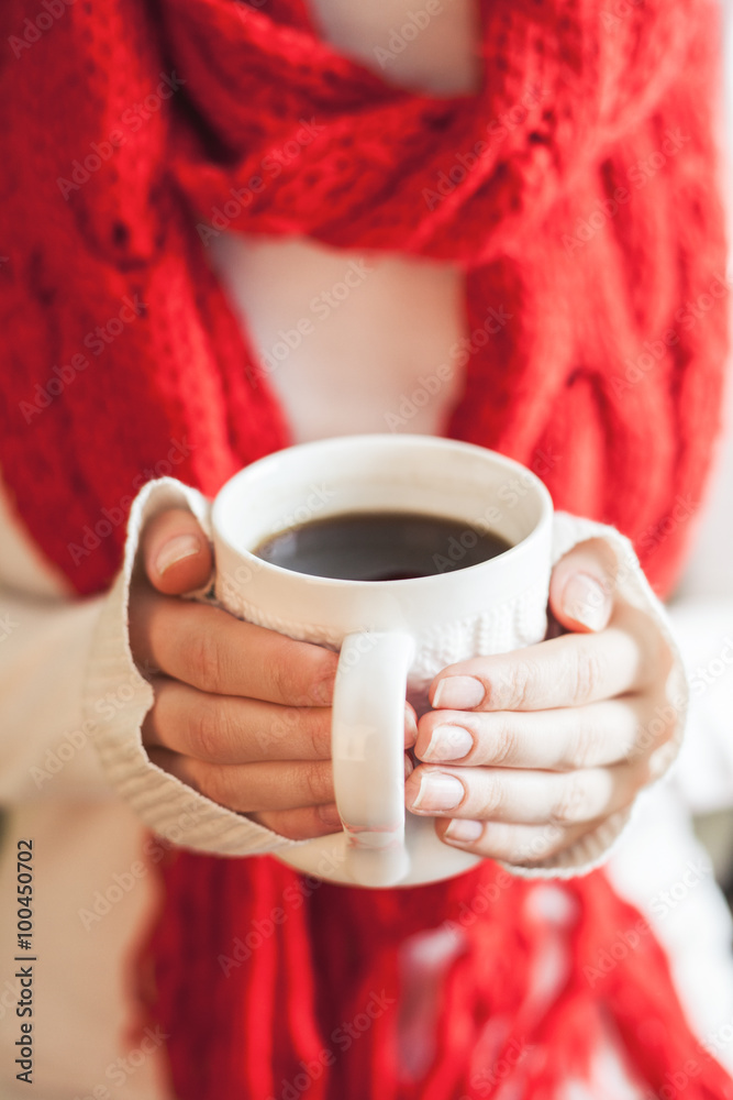 Woman hands in teal gloves holding a mug with hot coffee.