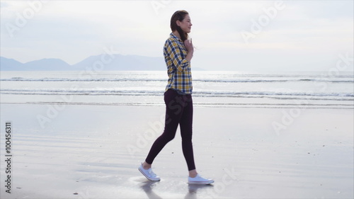 Slow motion video of young woman walking on beach. Full length side view of beautiful female in casual wear. Tracking shot of woman enjoying nature. Waves are rushing towards shore in background.