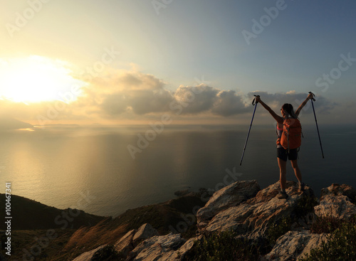 cheering young woman backpacker at sunrise seaside mountain peak