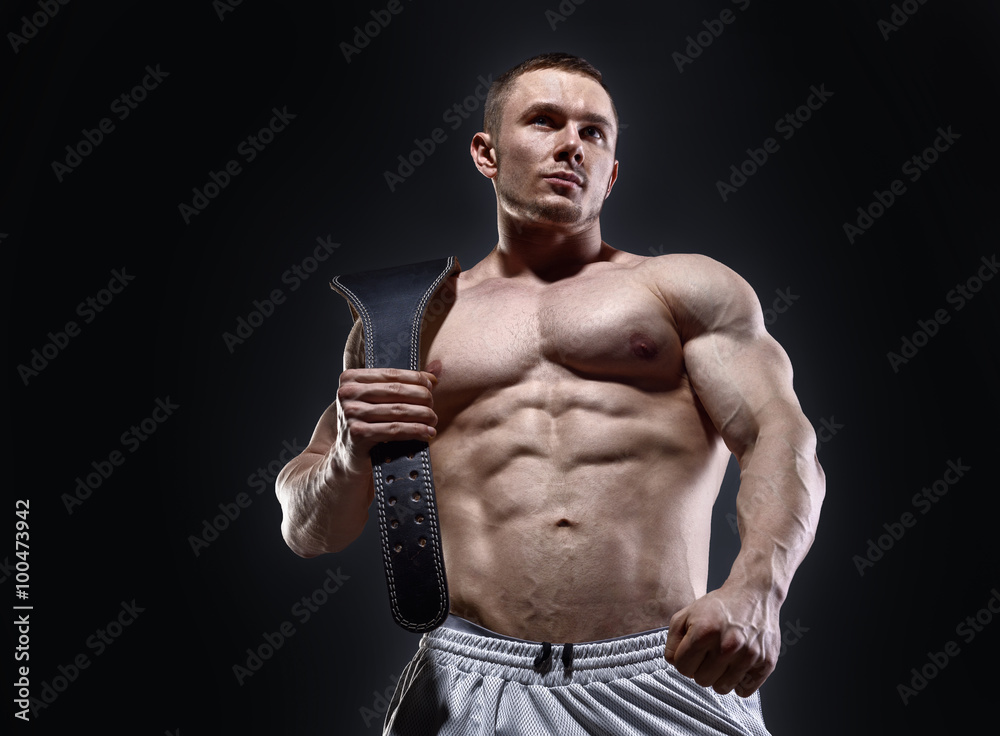 Muscular man in with lifting belt posing over dark background
