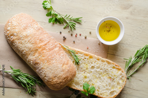 Sliced bread ciabatta watered with extra virgin olive oil with herbs on wooden background. View from above.