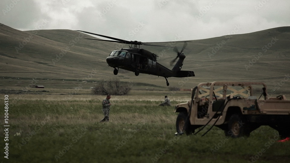 Helicopter landing in field with surrounding Humvee and soldiers